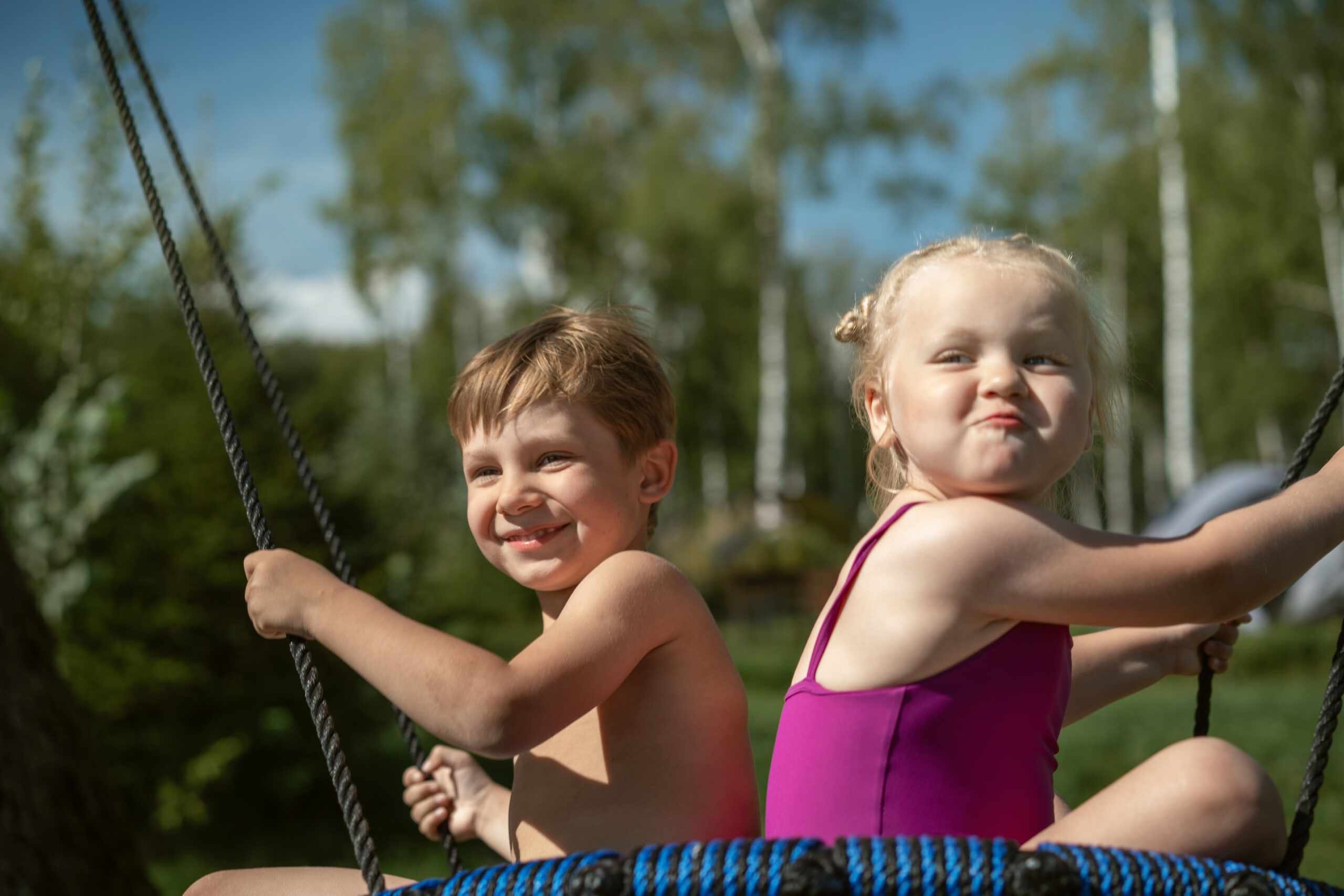 cute little boy and girl having fun on a spiderweb tree swing at playground. summer vacation in the nature.