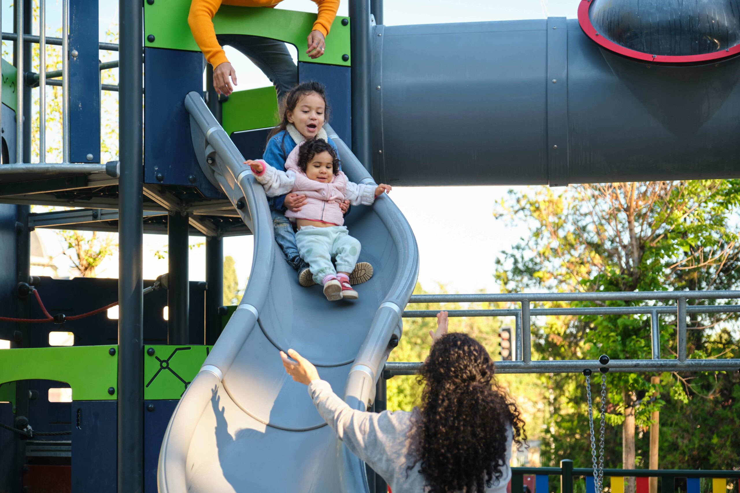 hispanic parents playing with her children at the slide in a park.